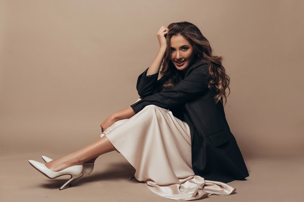 cheerful-model-sitting-floor-wearing-modern-oversize-black-jacket-creamy-long-dress-high-heel-shoes-her-feet-curly-hairstyle-makeup_343629-61